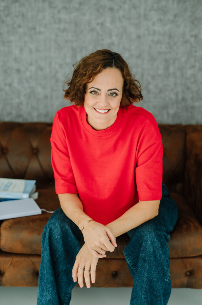 Coach Susan Zotz auf einer Couch im roten Oberteil